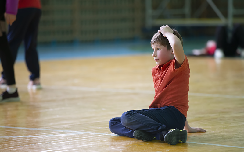 Young boy sits on gymnasium floor doing a stretch