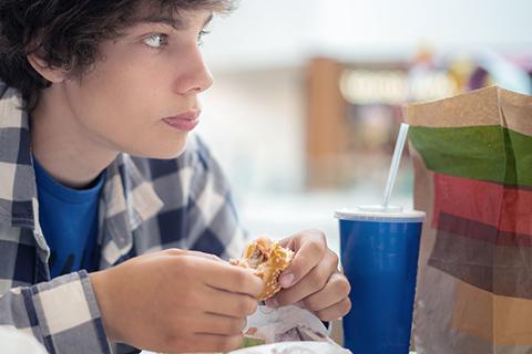 Boy sits at lunch with fast-food bag and drink in paper cup