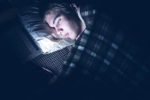 Child lay in bed while looking at lit-up smartphone