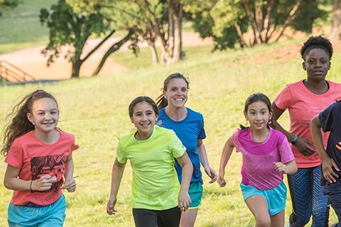 Five children are running across park grass