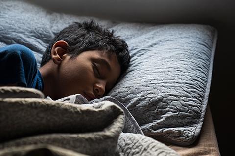 Child under sheet rests head on pillow